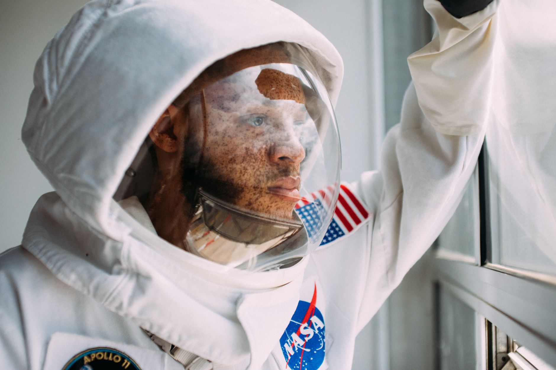 African American man in a NASA space suit peers out a window, capturing a moment of reflection and exploration.