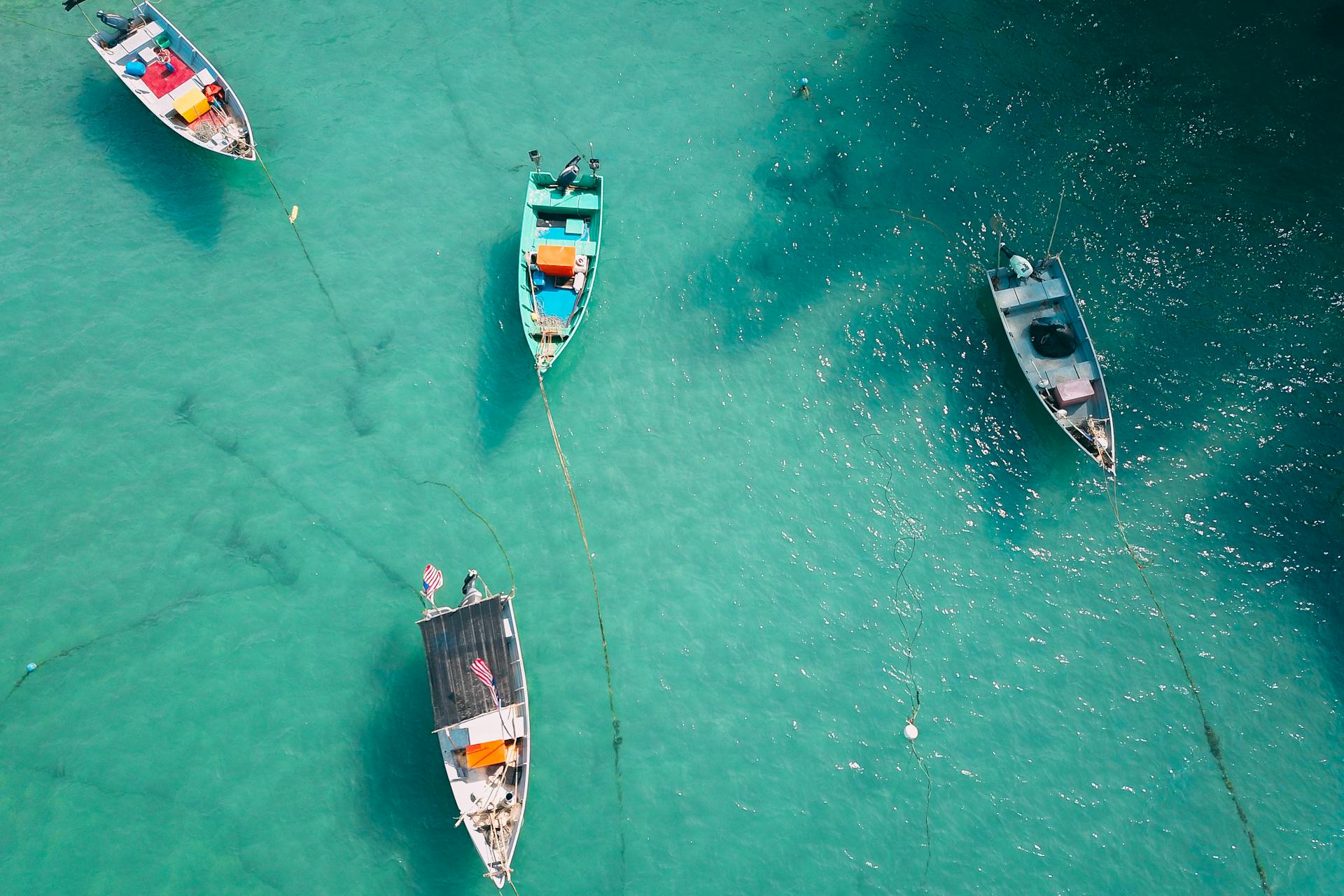 From above of small boats with motors floating on turquoise water near shore in sunny day