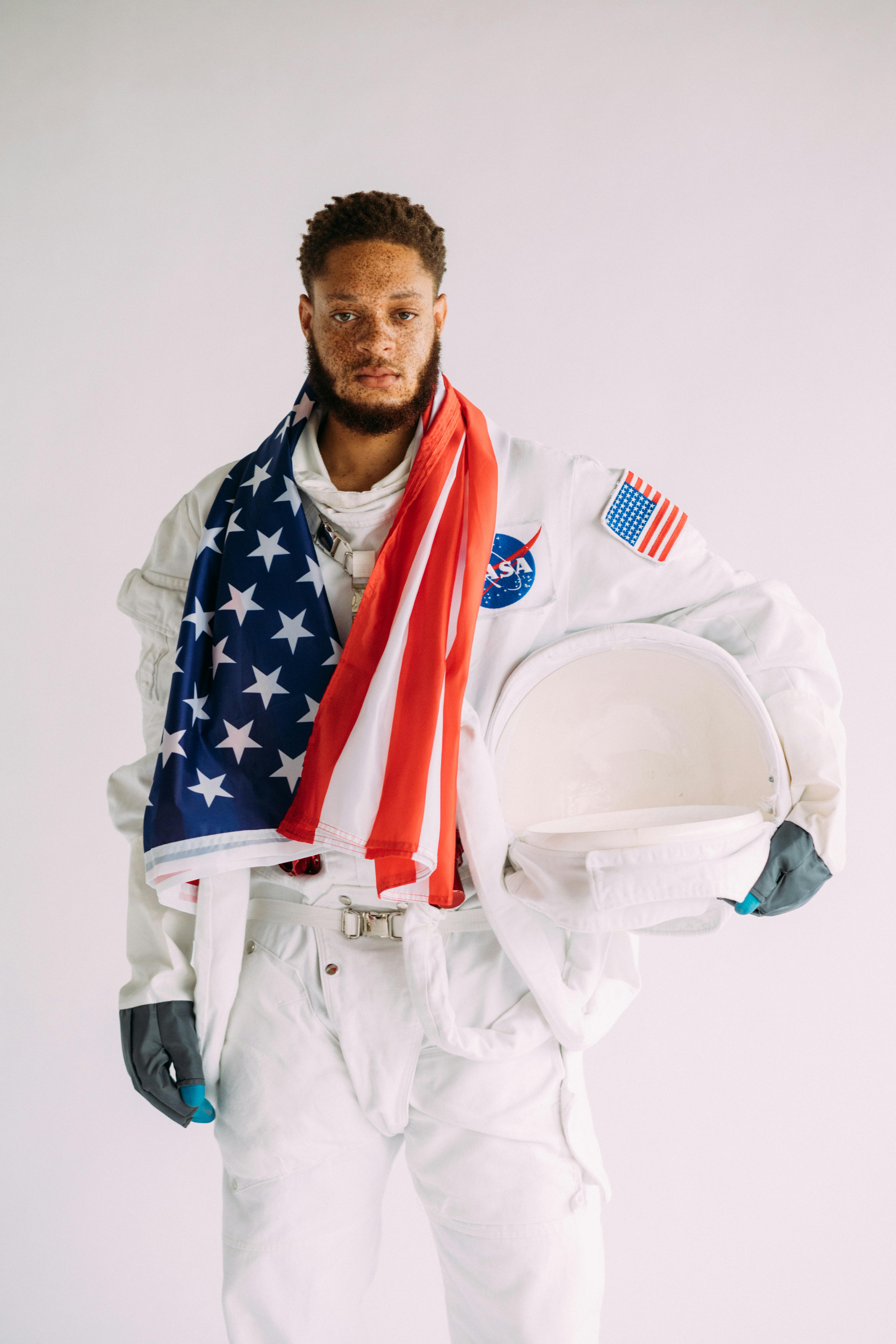 宇航员穿着太空服，戴着头盔，头盔上覆盖着美国国旗，背景为白色