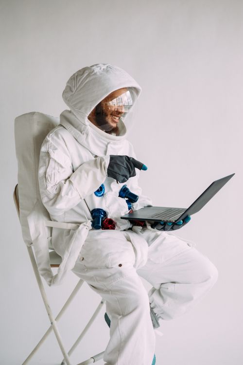 Free Man wearing astronaut costume using laptop indoors, showcasing a unique blend of space theme and technology. Stock Photo