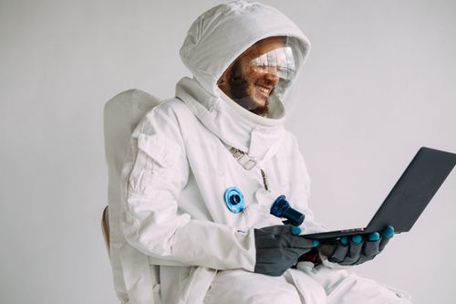 Free Smiling man in astronaut suit using a laptop indoors. Perfect for sci-fi and technology themes. Stock Photo