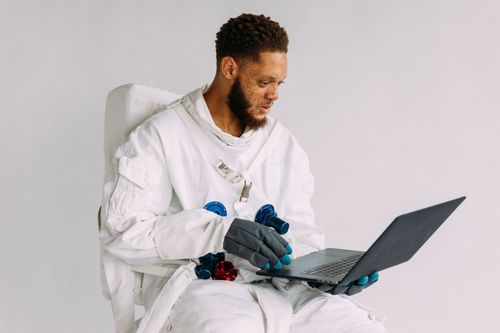 Free An astronaut in a space suit operating a laptop indoors, conveying technological themes. Stock Photo
