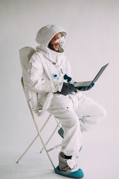 一位身穿白色宇航服的宇航员正坐在椅子上使用笔记本电脑，背景是白色的
