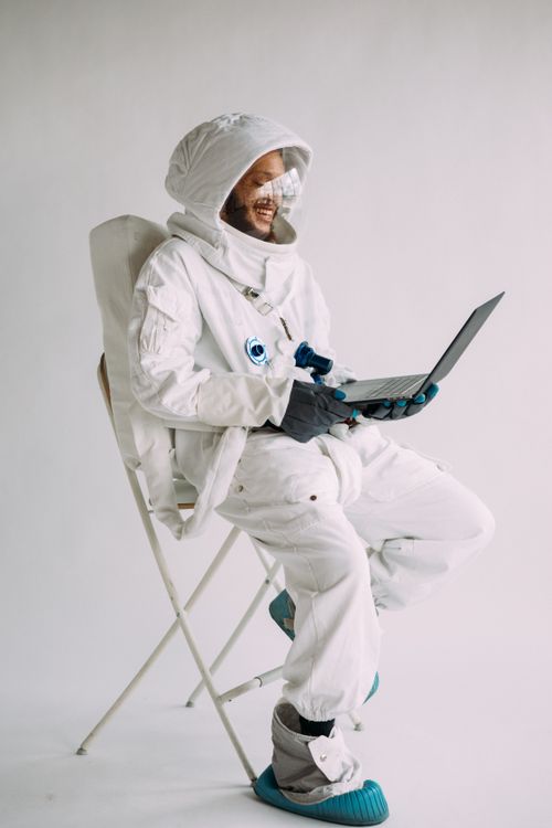 Free Astronaut in a white spacesuit sits on a chair using a laptop against a white background. Stock Photo
