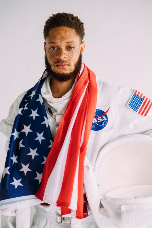Free Portrait of an African American astronaut wearing a NASA space suit and holding the USA flag. Stock Photo