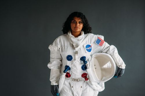 Free Woman dressed as astronaut holding helmet in NASA suit against grey background. Stock Photo