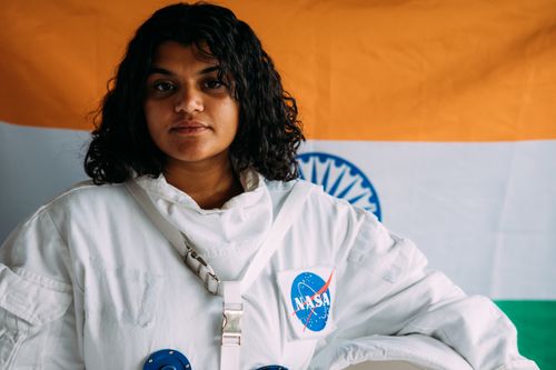 Free Portrait of an Indian woman wearing a NASA space suit and standing in front of the Indian flag. Stock Photo