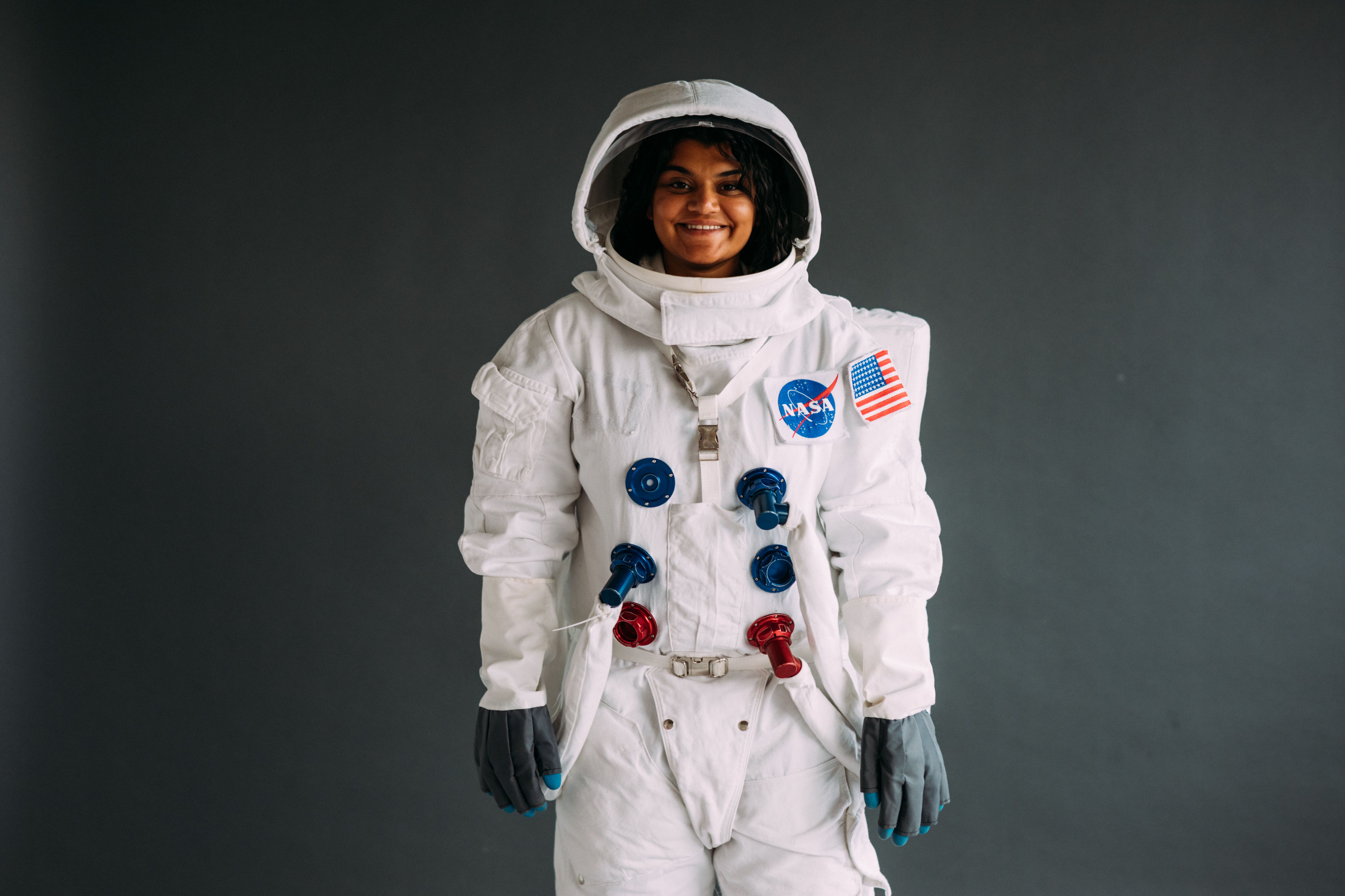 Female astronaut in NASA spacesuit standing against a dark background