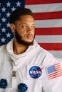 一名身穿美国宇航局太空服的男子站在美国国旗前，望向旁边