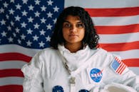 一名女子身穿美国宇航局宇航员服，在美国国旗背景下自信地摆出姿势