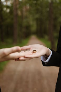 Close-up of hands exchanging a gold ring outdoors in a forest setting, symbolizing love and commitment.