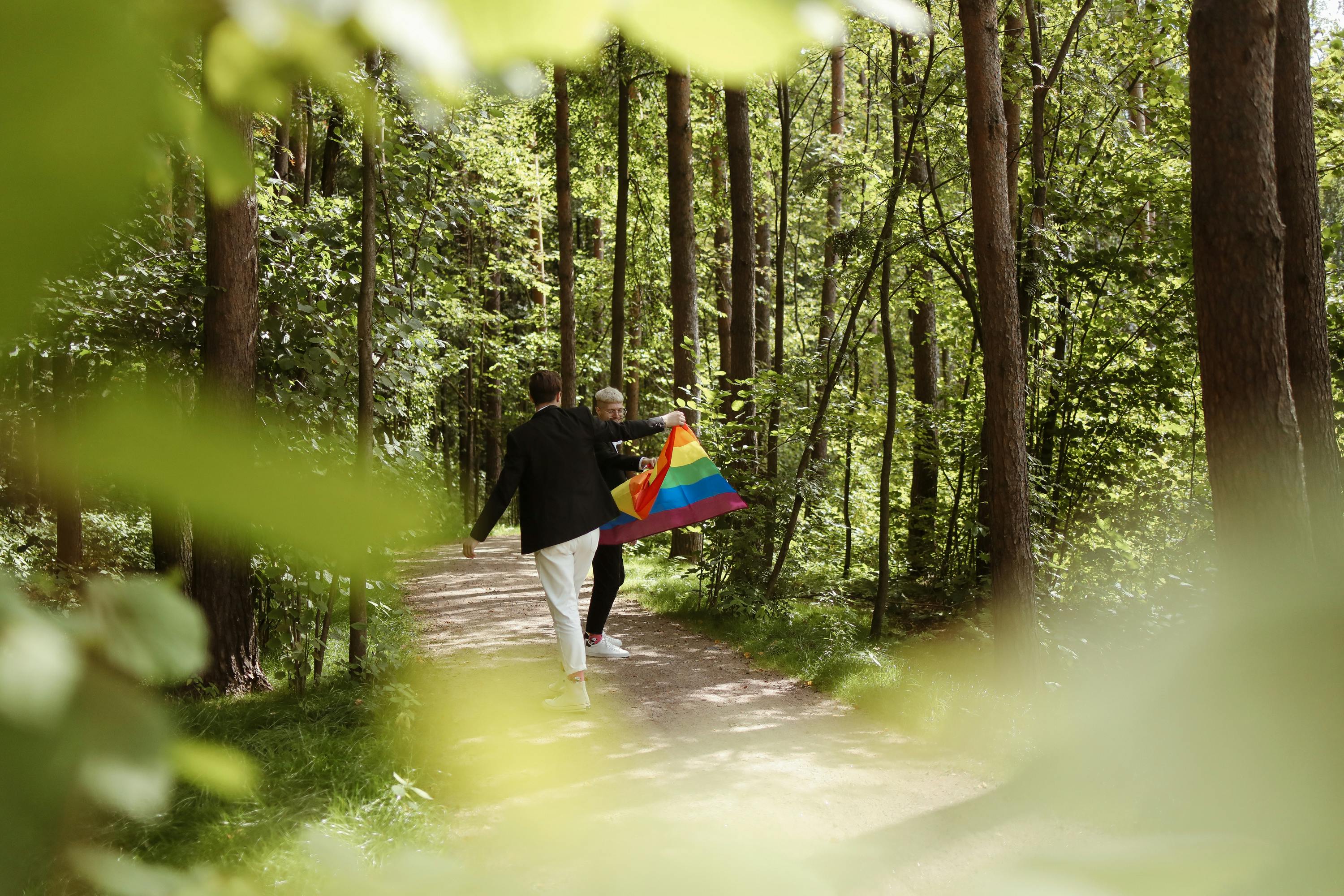 两名男子举着彩虹旗，一同走在森林中，象征着爱与多样性