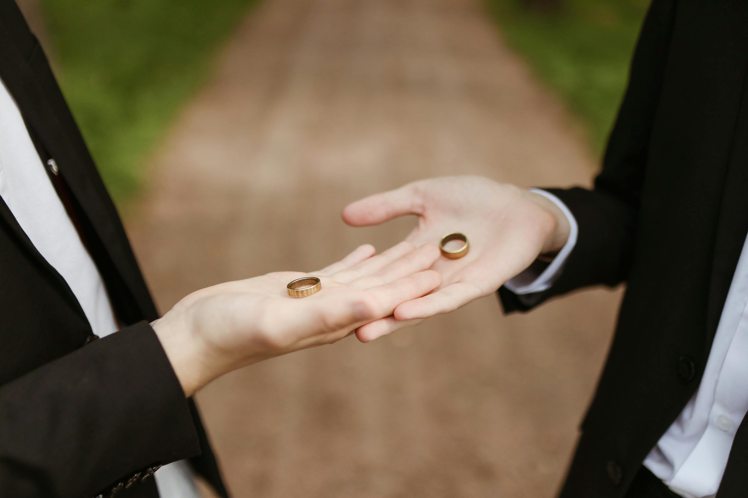 Close-up of two people exchanging wedding rings outdoors, symbolizing commitment.