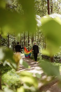 一对夫妇举着彩虹旗，走在阳光明媚的森林小路上