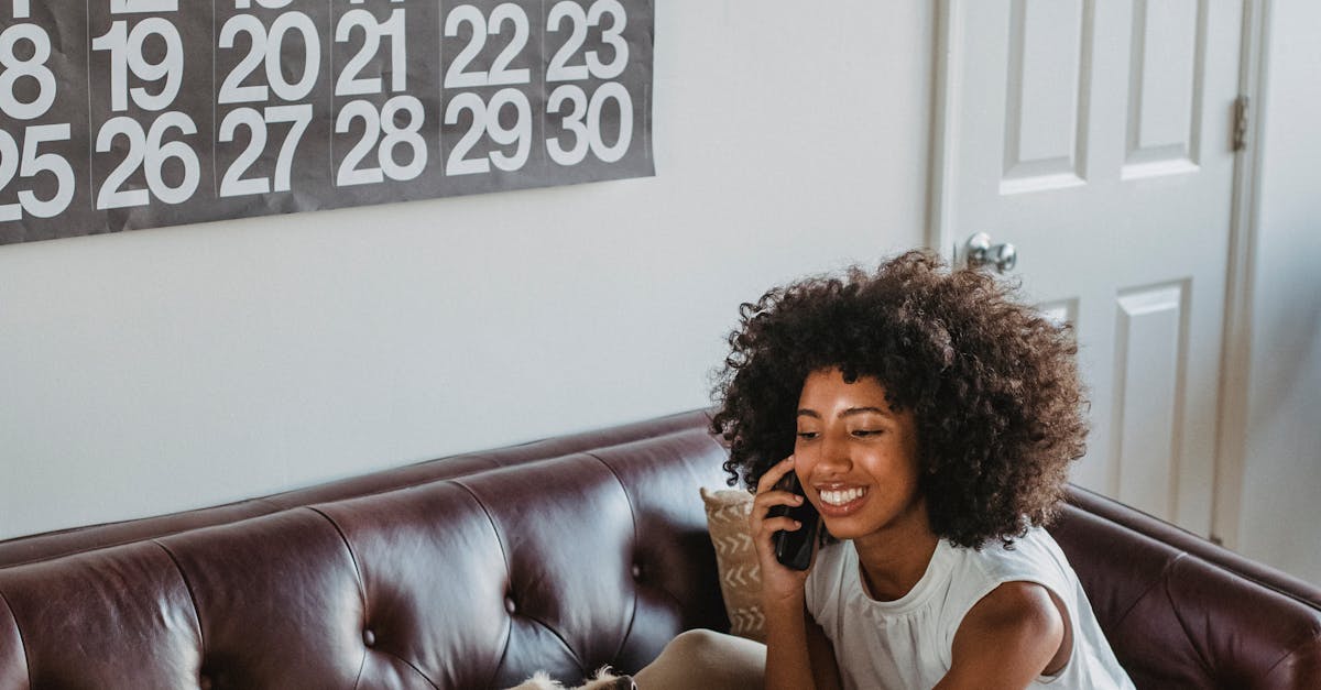 Cheerful black woman speaking on smartphone while caressing dog indoors