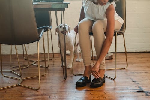 Black woman putting on shoes sitting on chair near dog