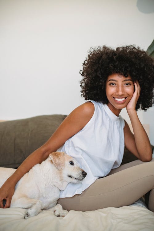 Cheerful black woman with pet resting on bed