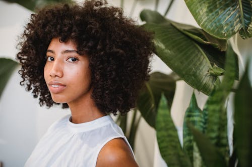 Positive black woman with curly hair near green plants