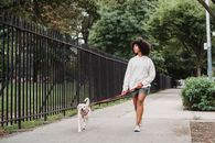 一名年轻女子牵着她的白狗，在城市公园的人行道上散步