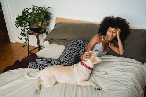 Happy black woman lying on bed with dog