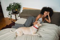 一位开朗的非洲发型女子和她的狗在室内的床上享受着舒适的时刻