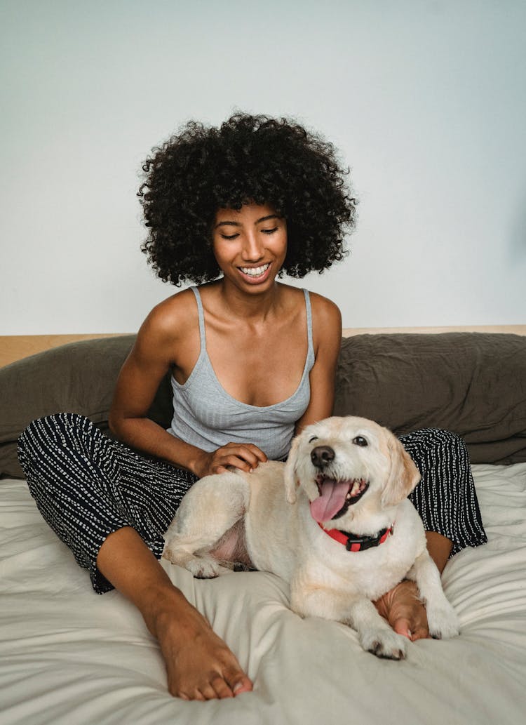 Black Woman With Playful Puppy On Bed