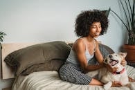 Smiling African American woman with curly hair resting on soft bed and stroking obedient dog in bedroom at home