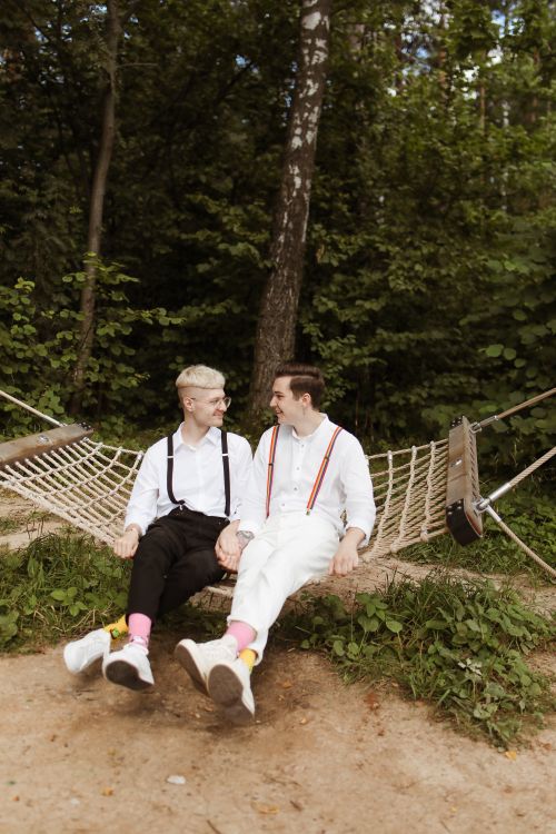 Free A happy couple sitting on a hammock in a lush outdoor setting, sharing a loving moment. Stock Photo