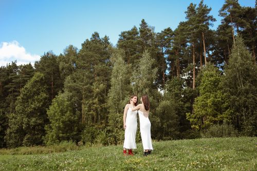 Free Two women in white dresses enjoying a romantic moment in a forest setting. Stock Photo