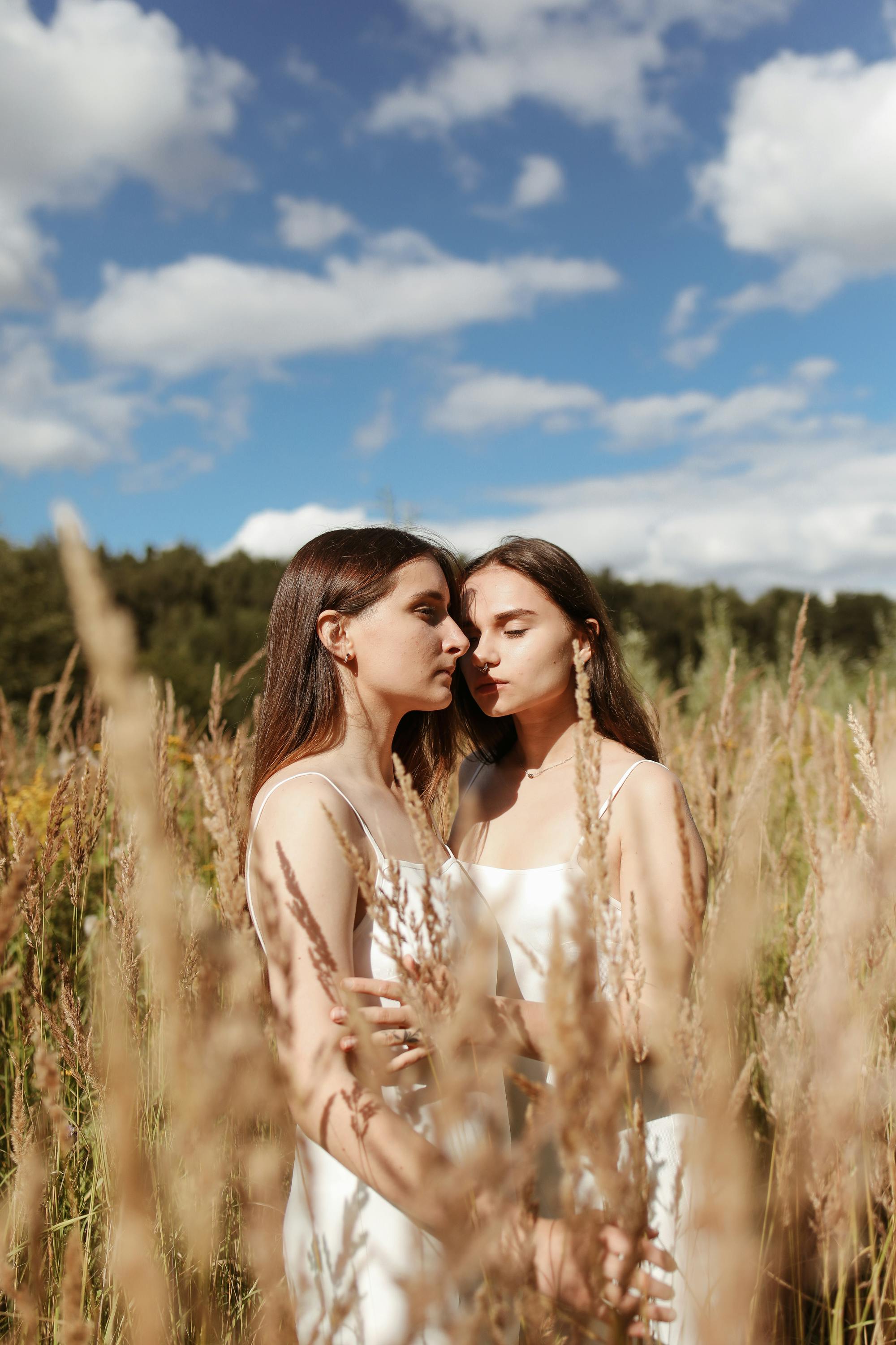两个穿着白色连衣裙的女人在阳光明媚的麦田里分享了亲密的时刻