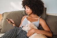 一位卷发的年轻女子躺在床上放松身心，旁边有狗和智能手机