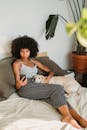 一位年轻黑人女性在家中舒适的床上休息，抱着可爱的狗玩手机
