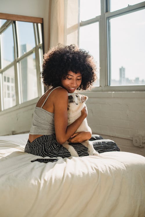 Smiling black woman embracing purebred dog on bed
