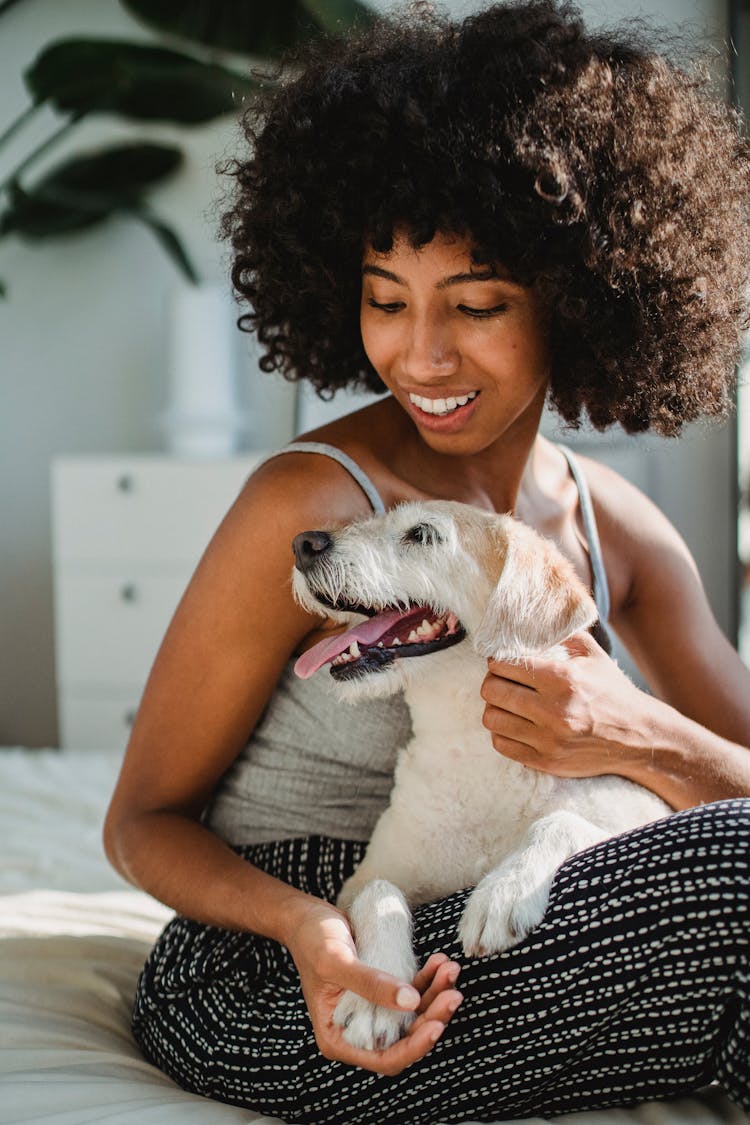 Happy Black Woman Cuddling Dog In Bedroom