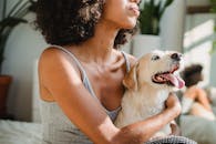 一位非洲裔美国女性在卧室里抱着可爱的纯种小狗，小狗吐着舌头，两人一同映在镜中