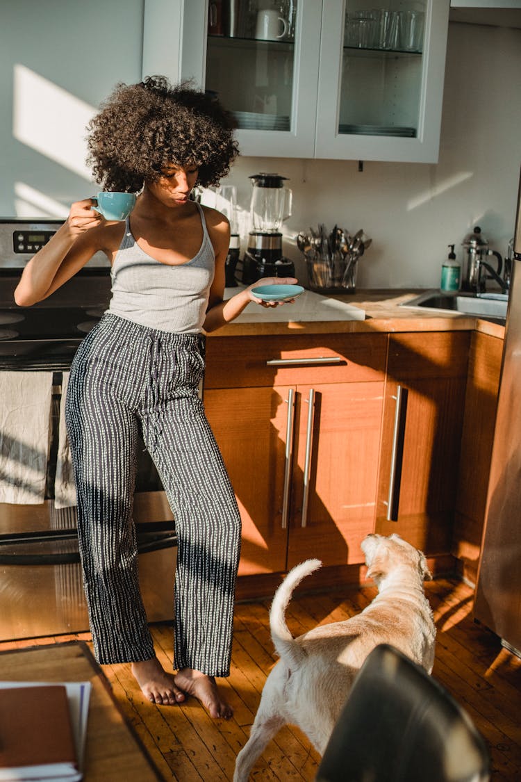 Black Woman With Coffee Near Purebred Dog In Kitchen