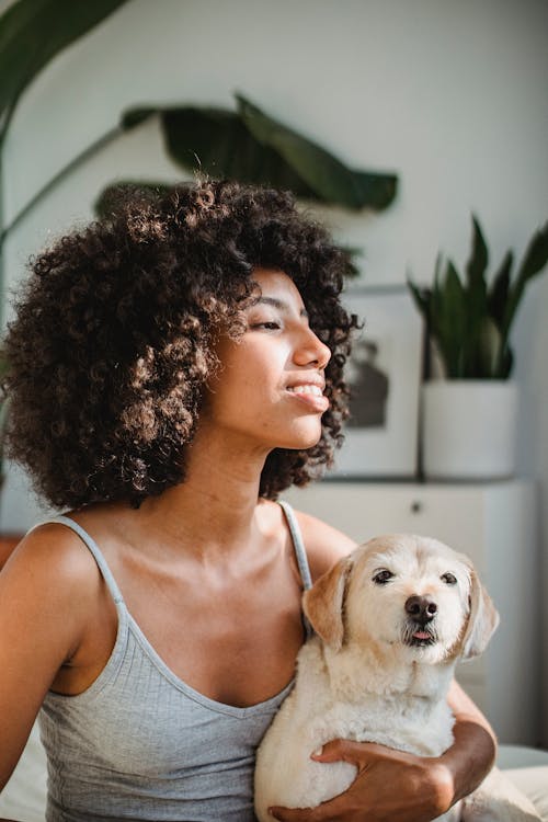 Smiling black woman embracing purebred puppy on bed at home