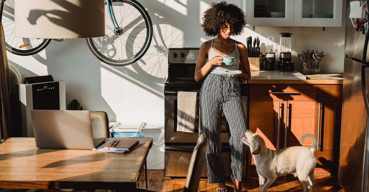 Young barefoot African American female with cup of hot drink standing on floor with dog at home