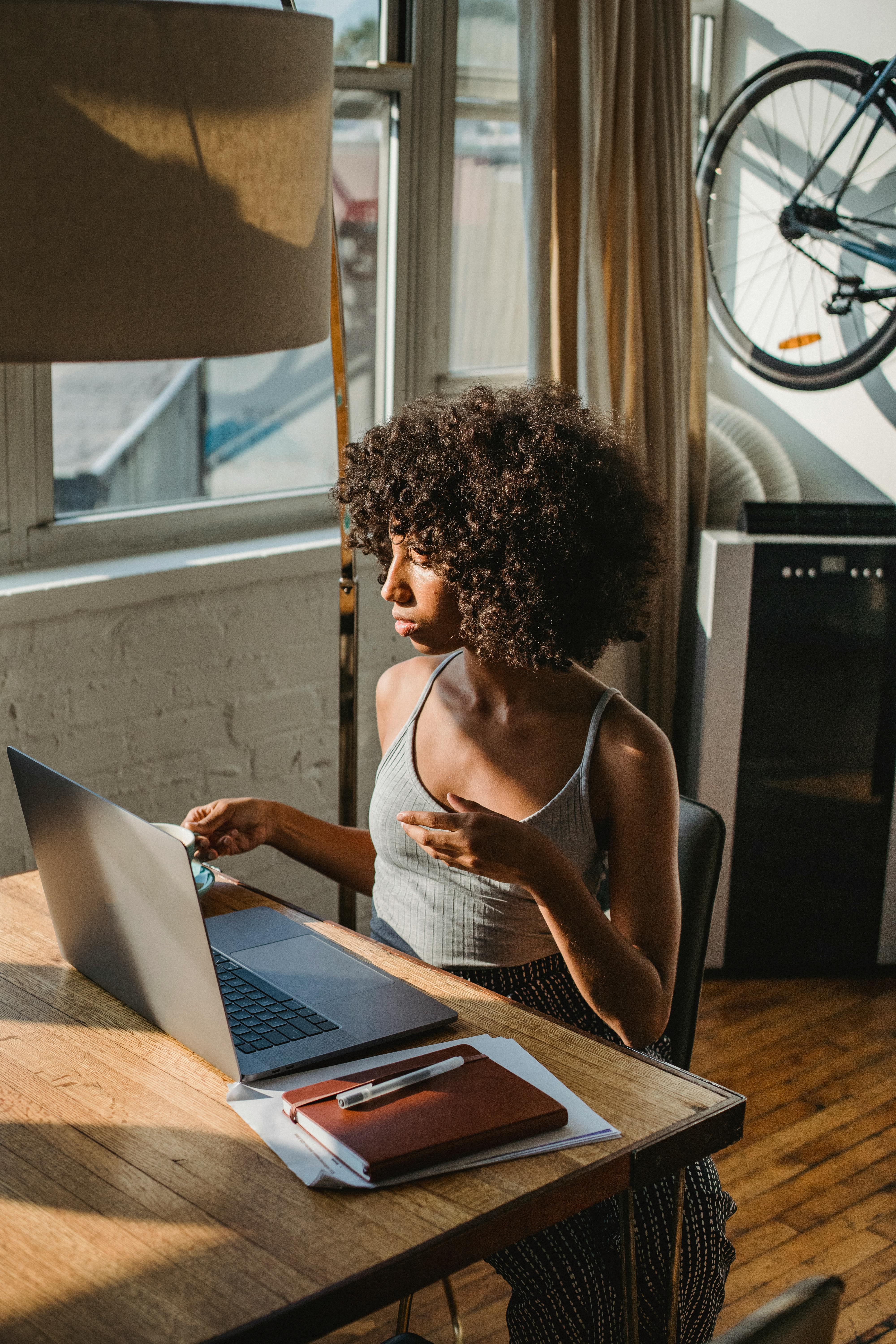 black remote worker with laptop and coffee at table indoors