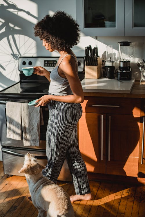 Black woman with coffee walking on floor with dog indoors