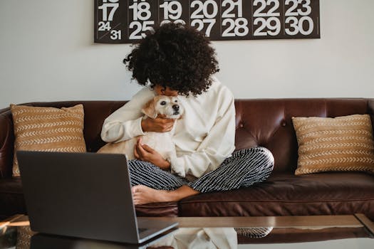 Woman in a cozy home office setting, hugging her dog while working remotely on a laptop.
