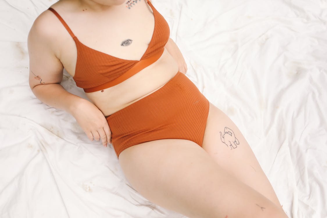 Free Tattooed Woman in Orange Lingerie Lying on White Blanket Stock Photo