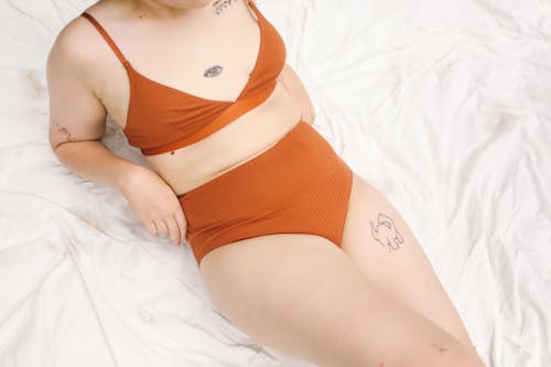 Free Tattooed Woman in Orange Lingerie Lying on White Blanket Stock Photo