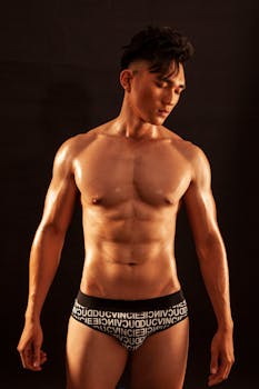 Shirtless male model displaying fit physique against a black background in a studio shoot.