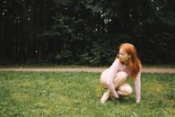 Woman in Beige Long Sleeve Shirt Sitting on Green Grass Field