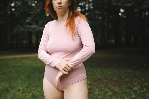 一位身穿粉色紧身衣的红发女子，在郁郁葱葱的公园里伸展双臂