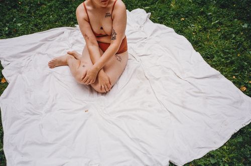 Free A woman with tattoos sits on a white blanket outdoors, relaxing in nature. Stock Photo