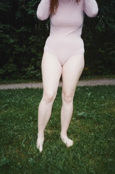 一名身穿粉红色服装的女子赤脚站在森林背景的草地上
