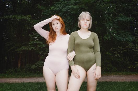 在郁郁葱葱的绿色背景下，两个穿着紧身衣的女人正积极拥抱彼此