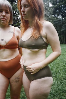 两名女子穿着泳衣，自信地在长满草地的户外摆姿势